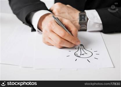business, marketing, planning and people concept - close up of male hands with pen drawing bulb on white paper