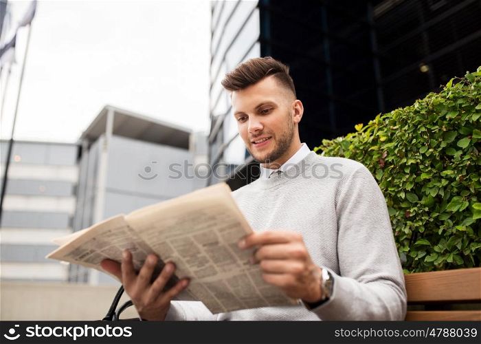 business, mass media and people concept - smiling man reading newspaper on city street bench