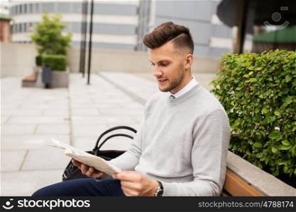 business, mass media and people concept - smiling man reading newspaper on city street bench