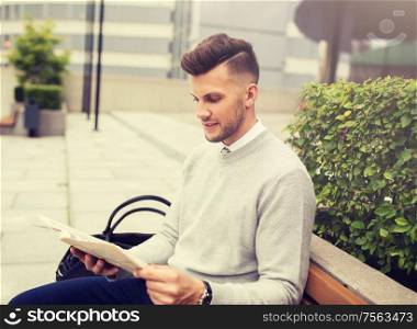business, mass media and people concept - smiling man reading newspaper on city street bench. smiling man reading newspaper on city street bench