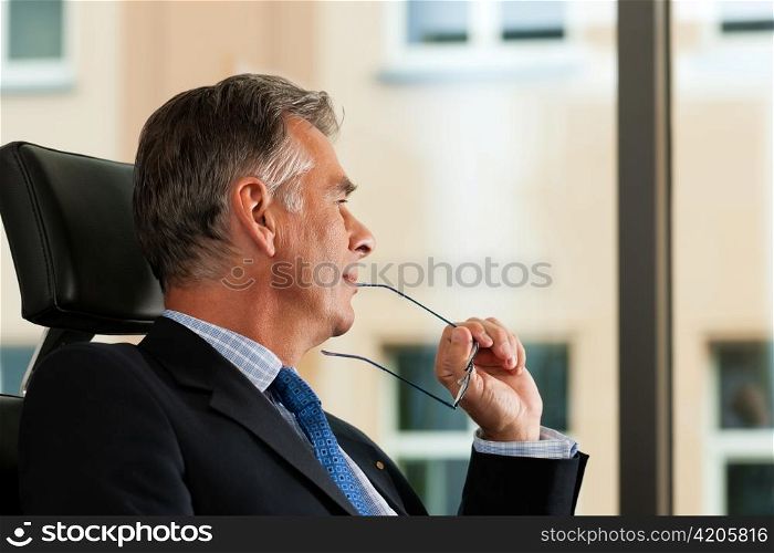 Business - mature boss contemplating in his office; he is looking out of the window