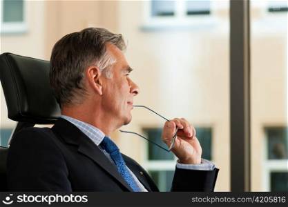 Business - mature boss contemplating in his office; he is looking out of the window