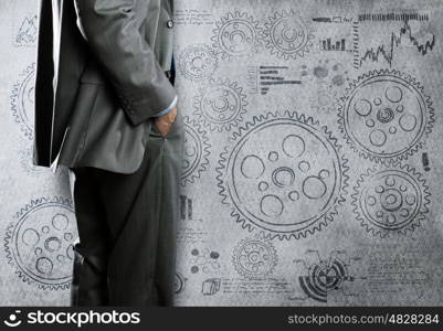 Business mechanisms. Bottom view of businessman and cogwheels on wall