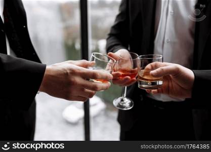 Business meeting. Men hold glasses of whiskey. Men’s Party. Hand with a drink of alcohol.. Business meeting. Men hold glasses of whiskey. Men’s Party. Hand with a drink of alcohol