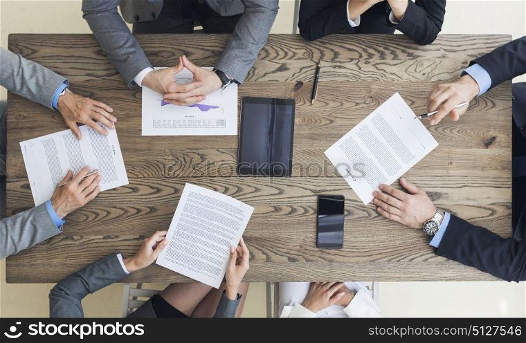 Business men discussing contract terms. Top view of confident business men in suits sitting at wooden table and discussing new contract terms before signing it