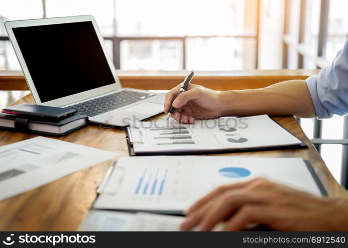 business men working on wooden desk(table) with notebook computer paper, pencil and hand in office, financial concept