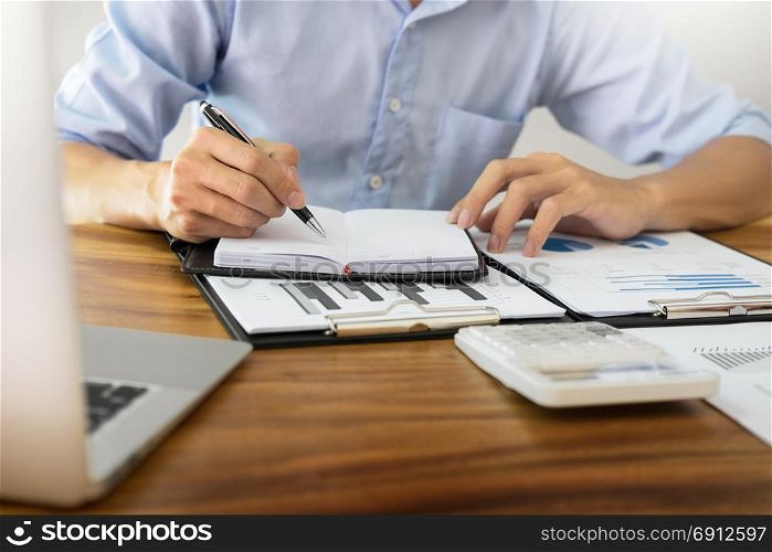 business men working on wooden desk(table) with notebook computer paper, pencil and hand in office, financial concept