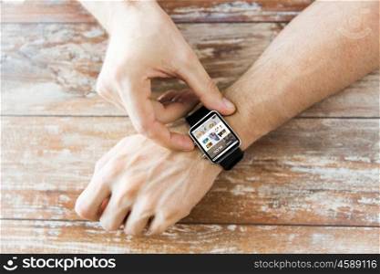business, modern technology, blogging, media and people concept - close up of male hands setting smart watch with internet blog on screen on wooden table