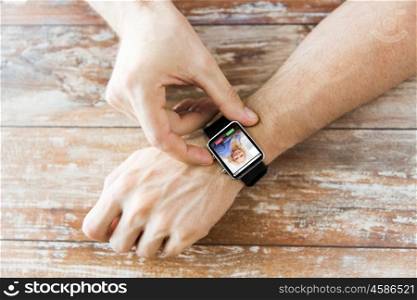 business, modern technology, communication and people concept - close up of male hands setting smart watch with incoming call on screen on wooden table