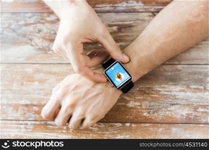 business, modern technology, media and people concept - close up of male hands setting smart watch with music player on screen on wooden table
