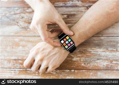 business, modern technology, media and people concept - close up of male hands setting smart watch with menu icons on screen on wooden table