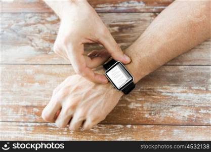 business, modern technology, programming and people concept - close up of male hands setting smart watch with coding on screen on wooden table