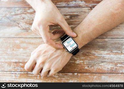 business, modern technology, social network, communication and people concept - close up of male hands setting smart watch with messenger on screen on wooden table