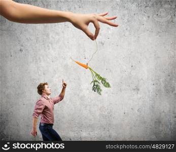Business motivation. Young man in casual teased by carrot hanging on rope