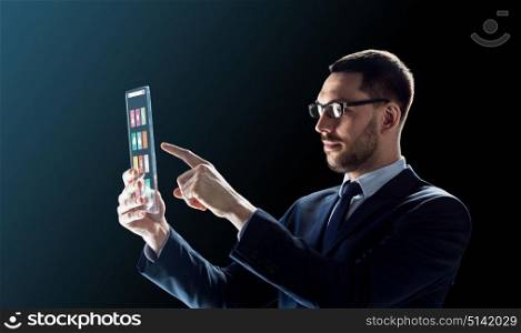 business, multimedia and future technology concept - businessman in glasses working with media icons on transparent tablet pc computer screen over black background. businessman working with transparent tablet pc