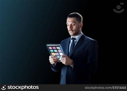 business, multimedia and future technology concept - businessman in suit working with media icons on transparent tablet pc computer screen over black background. businessman working with transparent tablet pc