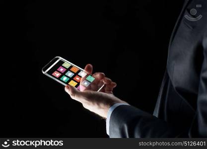 business, multimedia, people and modern technology concept - close up of businessman hand with transparent smartphone with menu icons on screen over black background. close up of businessman hand with glass smartphone