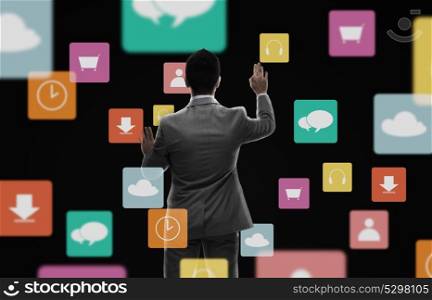 business, multimedia, people and technology concept - businessman working with virtual icons from back over black background. businessman working with virtual icons over black