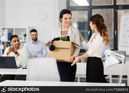 business, new job and corporate concept - female office worker with box of personal stuff and happy smiling colleague. new female employee meeting colleagues at office