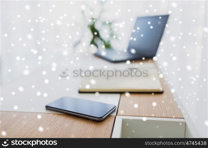 business, objects and education concept - office workplace with notebook, laptop computer and smartphone on table over snow