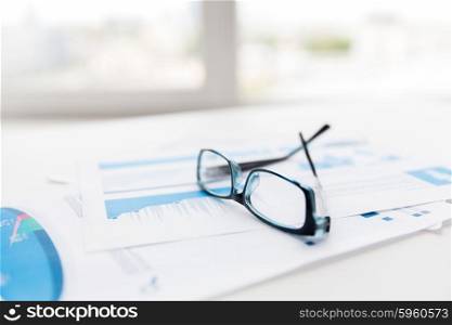 business, objects and statistics concept - close up of eyeglasses and files on office table