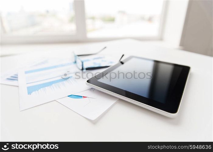 business, objects and technology concept - close up of tablet pc computer, eyeglasses and papers on office table