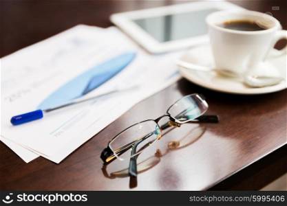 business, office and objects concept - close up of eyeglasses, tablet pc, charts and coffee on table
