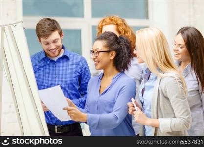 business, office and startup concept - smiling business team with flip board having discussion in office