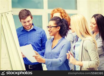 business, office and startup concept - smiling business team with flip board having discussion in office