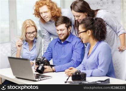 business, office and startup concept - smiling creative team with laptop computer and photocameras working in office
