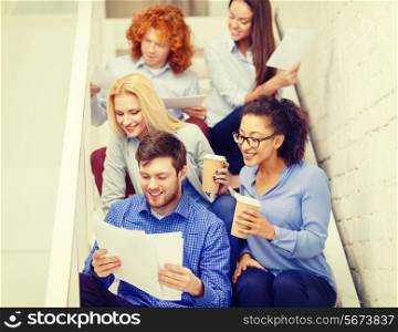business, office and startup concept - smiling creative team with papers and take away coffee on staircase