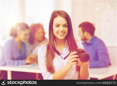 business, office and startup concept - smiling female photographer with photocamera in office with team on the back