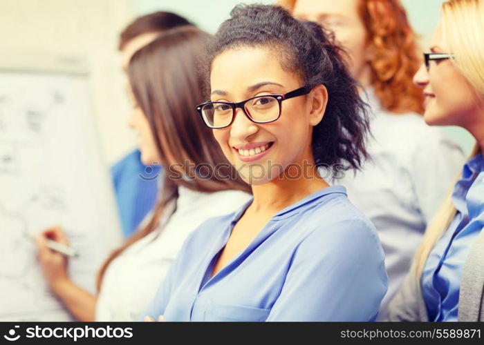 business, office and startup concept - smiling smiling businesswoman in eyeglasses with team team on the back