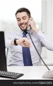 business, office and technology concept - smiling businessman making call and looking at wristwatch at office