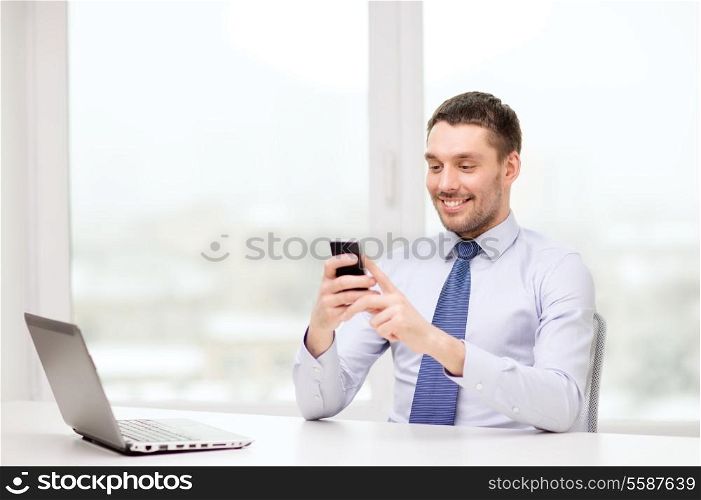 business, office and technology concept - smiling businessman with laptop computer and smartphone at office