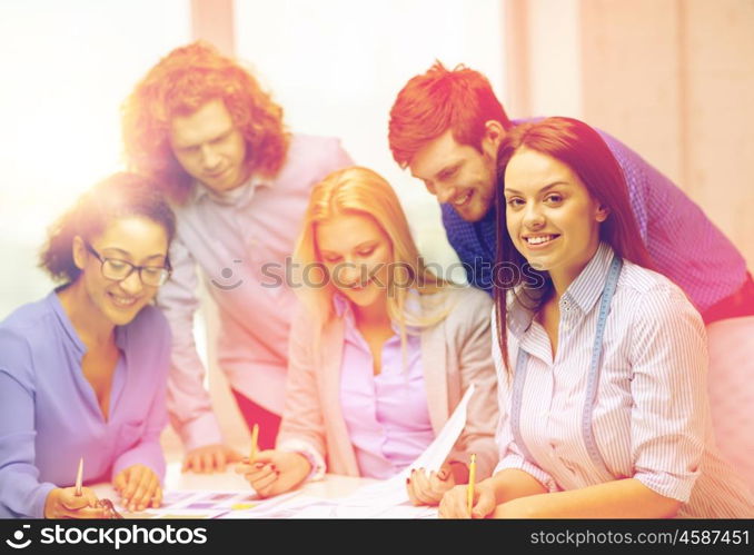 business, office, clothes design and starup concept - smiling female tailor with team on the back looking over clothes designs