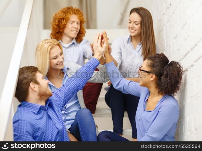 business, office, gesture and startup concept - smiling creative team doing high five gesture sitting on staircase