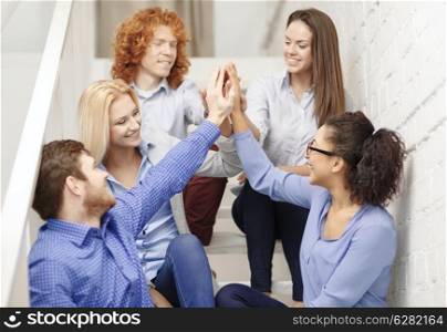 business, office, gesture and startup concept - smiling creative team doing high five gesture sitting on staircase
