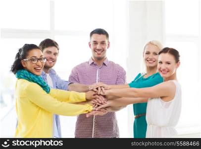 business, office, gesture and startup concept - smiling creative team with hands on top of each other sitting in office