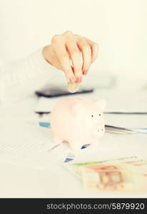 business, office, household, school, tax and education concept - woman hand putting coin into small piggy bank