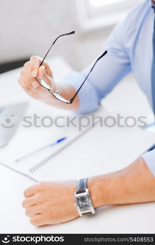 business, office, school and education concept - businessman with spectacles writing in notebook