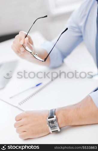 business, office, school and education concept - businessman with spectacles writing in notebook