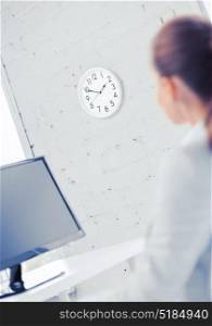business, office, school and education concept - businesswoman looking at wall clock in office. businesswoman looking at wall clock in office