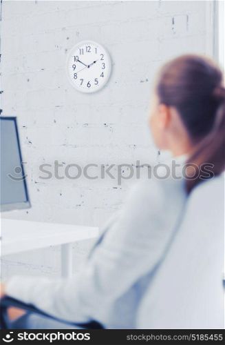 business, office, school and education concept - businesswoman looking at wall clock in office. businesswoman looking at wall clock in office