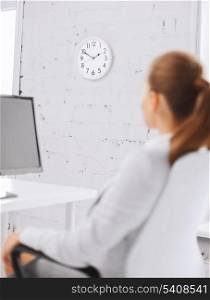 business, office, school and education concept - businesswoman looking at wall clock in office