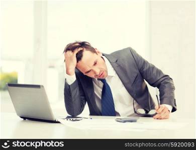 business, office, school and education concept - stressed businessman with laptop computer, papers and calculator