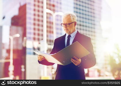 business, office work and people and concept - senior businessman paging documents in ring binder folder on city street. senior businessman with ring binder folder in city