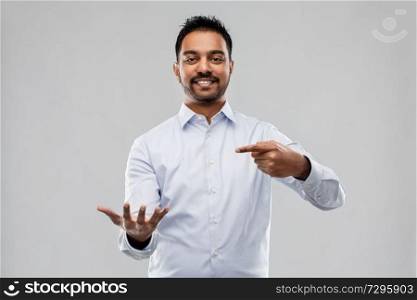 business, office worker and people concept - smiling indian businessman holding something invisible over grey background. indian businessman holding something invisible