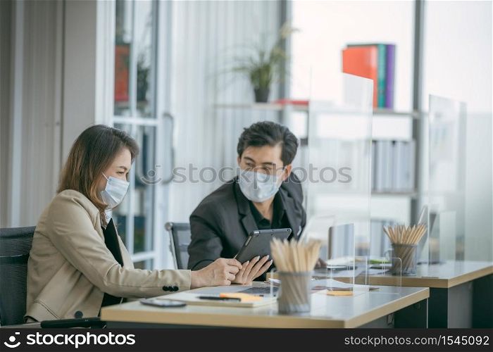 Business office working together at new normal social distance with table shield partition reduce infection of coronavirus covid-19 pandemic. Social and business distancing new normal lifestyle.