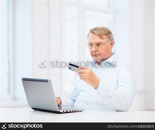 business, online banking, internet shopping and oldness concept - smiling old man with laptop computer and credit card at home